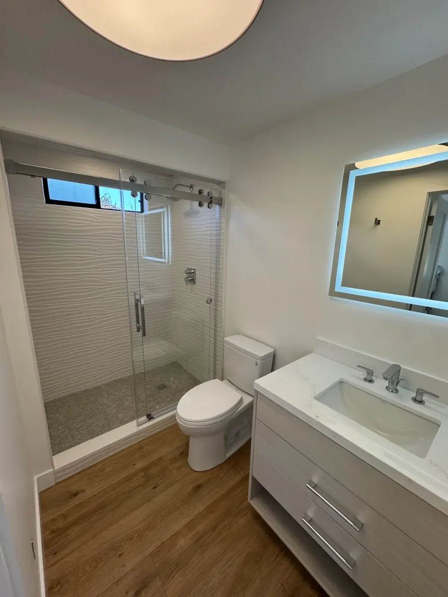 Complete bathroom remodel with glass shower, LED mirror, and wood-look flooring
