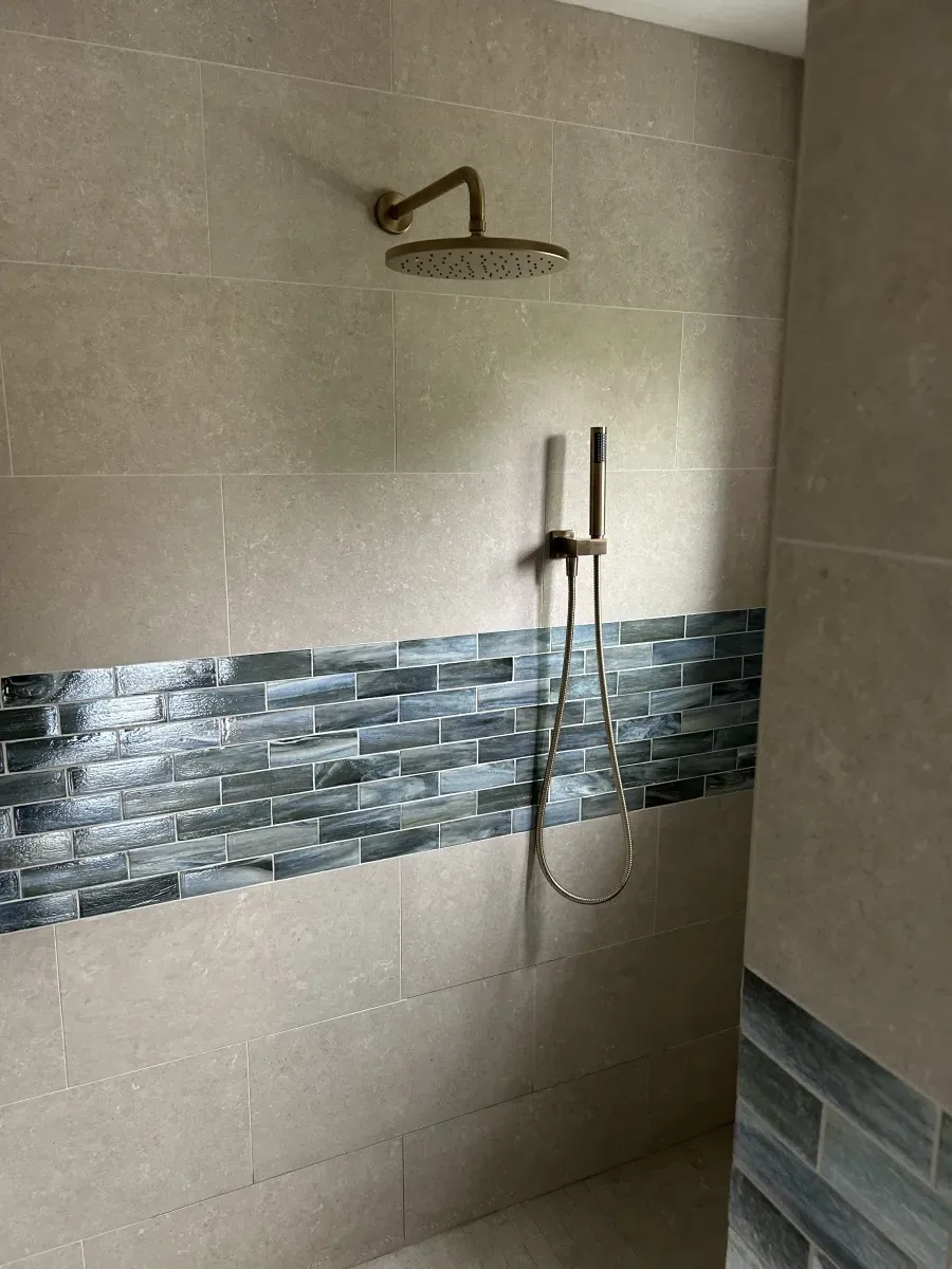 Walk-in shower with brushed gold rain head and accent tile stripe