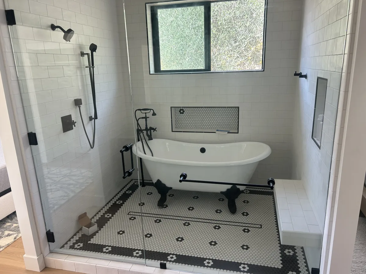 Clawfoot bathtub in glass-enclosed wet room with mosaic tile floor